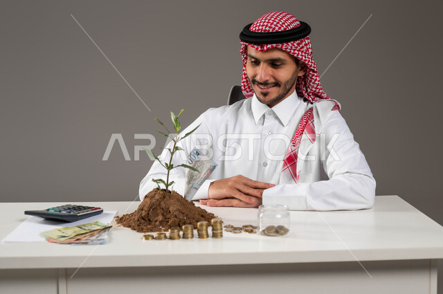 التخطيط في تمويل المشاريع المستقبلية, وظائف ومهن سعودية, بورتريه لرجل عربي خليجي سعودي مبتسم يرتدي الثوب التقليدي والشماغ ينظر إلى النبتة والتربة الخصبة بإيماءات السرور والسعادة بالإدخار المالي, الاستثمار في الاقتصاد السعودي, مفهوم الوفرة المالية, خلفية رمادية