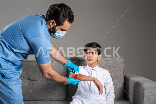 Expressions of sadness and pain, a portrait of a Saudi Arabian Gulf first aid nurse wearing a medical uniform, sterilizing the wounds of a boy on the sofa at home, health problems and physical injuries, urgent emergency health cases, the concept of home medical services and care, gray background