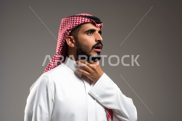 إيماءات التعب والألم وطلب المساعدة، التهاب اللوز والحاجة للمضادات الحيوية، بورتريه مقرب لرجل عربي سعودي خليجي يرتدي الشماغ والثوب التقليدي يضع يده على حنجرته ويقوم بالسعال, خلفية رمادية