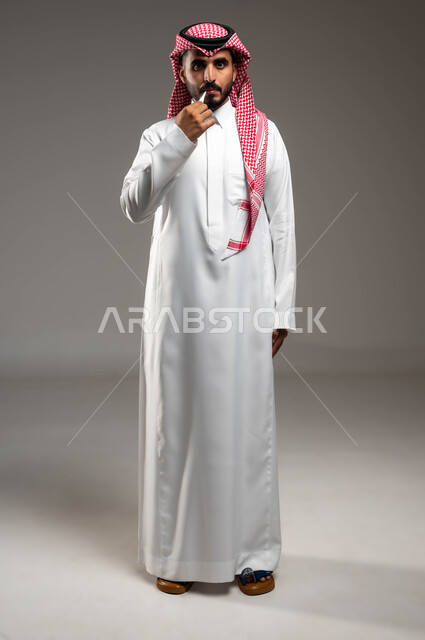 النظر الى الكاميرا بإيماءات الإرهاق بسبب المرض، الشعور بالتعب والإرهاق، بورتريه لرجل عربي سعودي خليجي يرتدي الشماغ والثوب التقليدي يقوم بقياس حرارته بإستخدام جهاز الميزان الرقمي, صورة الجسم بالطول الكامل، خلفية رمادية