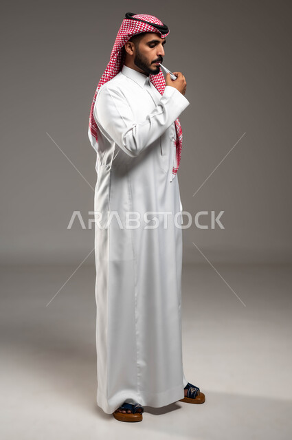 الحاجة إلى زيارة الطبيب للمساعدة ووضع خطة علاجية, الإصابة بالحمى والإرهاق، بورتريه لرجل عربي سعودي خليجي يرتدي الشماغ والثوب التقليدي يقوم بقياس حرارته باستخدام الميزان الرقمي، إيماءات التعب بسبب المرض, صورة الجسم بالكامل، خلفية رمادية