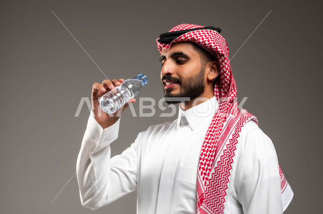 التخلص من سموم الجسم، أهمية شرب الماء النقي للمحافظة على بشرة نضرة، بورتريه مقرب لرجل عربي خليجي سعودي يرتدي الشماغ والثوب التقليدي يقوب بشرب المياه من عبوة بلاستيكية، المحافظة على سلامة الجهاز المناعي، الحفاظ على صحة الكلى ومعالجتها، خلفية رمادية