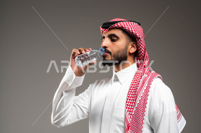 أهمية شرب الماء النقي للمحافظة على بشرة نضرة، بورتريه مقرب لرجل عربي خليجي سعودي يرتدي الشماغ والثوب التقليدي يقوب بشرب المياه من عبوة بلاستيكية، المحافظة على سلامة الجهاز المناعي، التخلص من سموم الجسم، الحفاظ على صحة الكلى ومعالجتها، خلفية رمادية