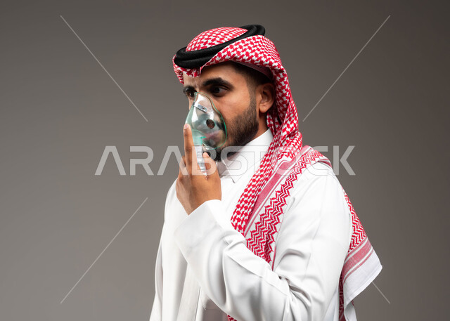 مداواة أمراض الربو المزمنة، المحافظة على ممر هوائي منتظم باستخدام جهاز التنفس الصناعي، بورتريه مقرب لرجل عربي سعودي خليجي يرتدي الشماغ والثوب التقليدي يقوم باستنشاق أدوية معالجة لانقطاع التنفس عن طريق قناع الاكسجين، تقديم الخدمات الصحية المنزلية، خلفية رمادية