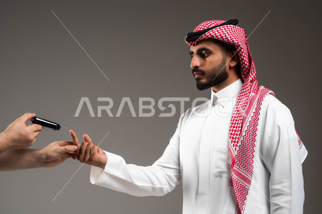 الفحص الطبي المنزلي والتشخيص السريع، بورتريه مقرب من الجانب لشاب عربي خليجي سعودي مريض يرتدي الشماغ والثوب التقليدي يقوم بقياس نسبة السكر في دمه باستخدام جهاز إلكتروني حديث لمرضى داء السكري، خلفية رمادية