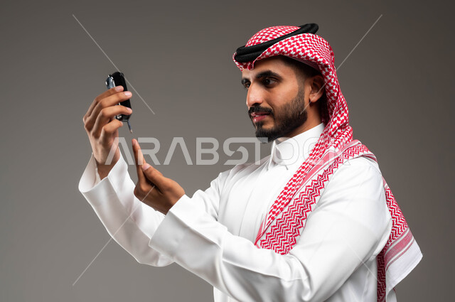 الفحص الطبي والتشخيص السريع في البيت، جهاز إلكتروني حديث لمرضى داء السكري في المنزل، بورتريه مقرب من الجانب لشاب عربي خليجي سعودي مريض يرتدي الشماغ والثوب التقليدي يقوم بفحص نسبة السكر في دمه، خلفية رمادية