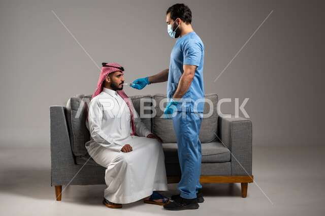 ممرض سعودي يرتدي الكفوف وكمامة الوقاية يقوم بقياس درجة حرارة الجسم بواسطة جهاز الترمومتر الرقمي، شركات التمريض المنزلي في السعودية, الحاجة إلى المساعدة الطبية, بورتريه لرجل مصاب بالحمى عربي خليجي سعودي يرتدي الثوب التقليدي والشماغ يجلس على الكنبة, خلفية رمادية