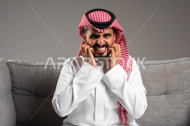 عدم التحمل والشعور بالآلام والأوجاع, بثور منتشرة على بشرة الوجه, المشاكل الصحية والإصابة بالحساسية الجلدية, الأمراض والتهجيات وفرط التحسس, بورتريه مقرب لرجل عربي خليجي سعودي يرتدي الثوب والشماغ التقليدي يضع يديه على وجهه بإيماءات الألم, خلفية رمادية