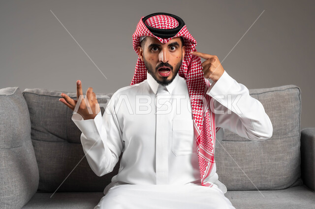 المشاكل الصحية وتهجيات الجلد, الإشارة إلى مكان الإصابة, بثور منتشرة على بشرة الوجه, بورتريه مقرب لرجل عربي خليجي سعودي يرتدي الثوب التقليدي والشماغ يرفع يديه بإيماءات السؤال والاستفسار, الإصابة بالحساسية الجلدية, خلفية رمادية