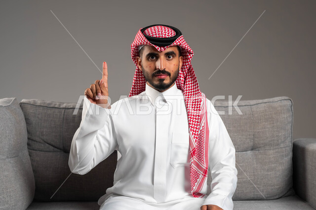 القيام بالتحاليل اللازمة, بورتريه لشاب عربي خليجي سعودي يرتدي الثوب والشماغ التقليدي يجلس على الكنبة ويرفع اصبعه السبابة للأعلى, المشاكل الصحية وتهيجات الجلد, بثور منتشرة على بشرة الوجه, الطفح الجلدي والأمراض المعدية, الإصابة الجلدية وفرط التحسس, خلفية رمادية