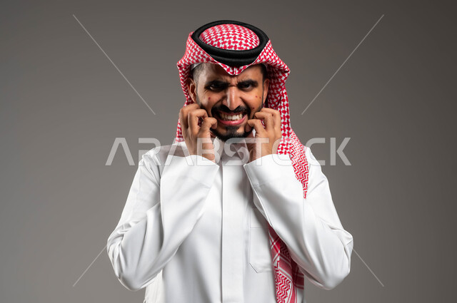 الشعور بالآلام والأوجاع وعدم التحمل, بثور منتشرة على بشرة الوجه, المشاكل الصحية والإصابة بالحساسية الجلدية, الأمراض والتهجيات وفرط التحسس, بورتريه مقرب لرجل عربي خليجي سعودي يرتدي الثوب والشماغ التقليدي يضع يديه على وجهه بإيماءات الألم والحكة, خلفية رمادية
