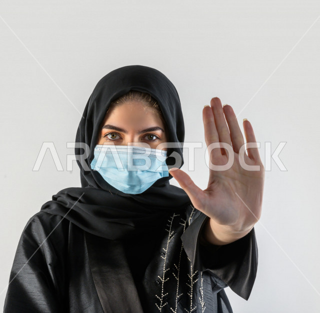 Portrait of a Saudi young woman wearing the muzzle to avoid the spread of the virus, follow safety measures by wearing gloves, avoid the spread of infection, white background