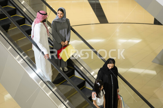 الاستفاده من العروض والتخفيضات الموسمية, سهولة الانتقال من طابق لآخر باستخدام السلالم الكهربائية, مجموعة من المواطنين العرب الخليجيين السعوديين يقومون باستخدام الدرج الكهربائي, متعه التسوق في المولات التجاريه واختيار المستلزمات والهدايا