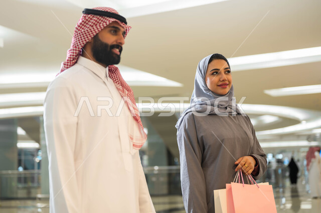 مشاركة الزوجين في اختيارات التسوق وتبادل الآراء, قضاء وقت ممتع في إحدى المولات التجارية في المملكة, صورة مقربة لرجل وامرأة عربيين سعوديين خليجيين في المرك التجاري في السعودية, الاستفاده من العروض والتخفيضات الموسمية
