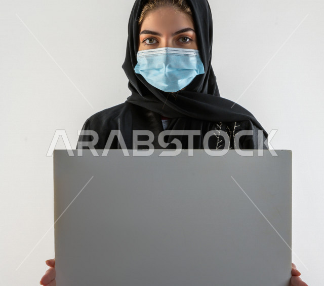 بورتريه لشابة سعودية تضع الكمامة ،  تحمل بيدها لوح ابيض فارغ ، اتباع اجراءات السلامة بوضع الكمامة بشكل صحيح ، تجنب انتشار العدوى ، خلفية بيضاء