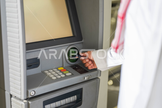 استخدام الوسائل والتقنيات الحديثة، صورة مقربة لرجل عربي خليجي سعودي يرتدي الزي التقليدي يقوم بإدخال البطاقة الائتمانية في ماكينة الصراف الآلي، سهولة وإمكانية سحب النقود، الدفع والشراء من خلال البطاقات البنكية