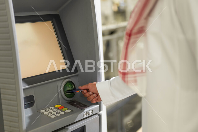 استخدام الوسائل والتقنيات الحديثة، صورة مقربة لرجل عربي خليجي سعودي يرتدي الزي التقليدي يقوم بإدخال البطاقة الائتمانية في ماكينة الصراف الآلي، سهولة وإمكانية سحب النقود، الدفع والشراء من خلال البطاقات البنكية