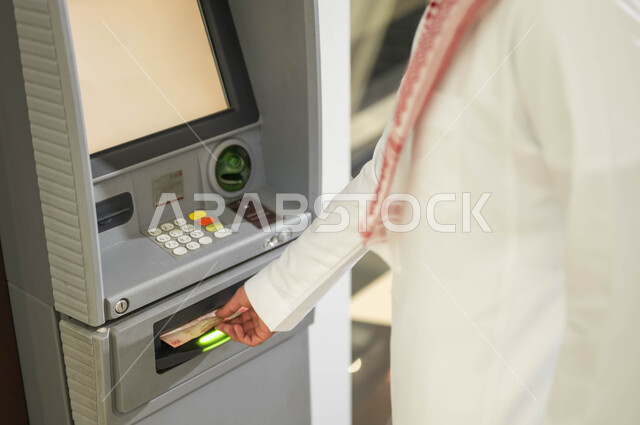 سهولة وإمكانية الشراء من خلال البطاقة الائتمانية، بطاقات الدفع الالكتروني والسحب الذاتي، استخدام الوسائل والتقنيات الحديثة، صورة مقربة لرجل عربي خليجي سعودي يرتدي الزي التقليدي يقوم بسحب النقود من ماكينة الصراف الآلي
