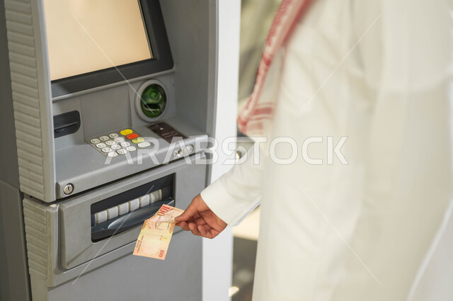 سهولة وإمكانية الشراء من خلال البطاقة الائتمانية، بطاقات الدفع الالكتروني والسحب الذاتي، استخدام الوسائل والتقنيات الحديثة، صورة مقربة لرجل عربي خليجي سعودي يرتدي الزي التقليدي يقوم بسحب النقود من ماكينة الصراف الآلي