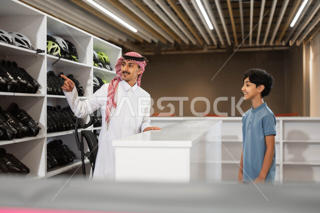 اجراء تجارب مثيرة و مميزة ،الاشارة الى شيء ما، استعارة الزلاجات وخوذة الحماية من الاستقبال عند مضمار التزلج، موظف عربي خليجي سعودي يقوم بمساعدة ولد في اختيار الأدوات اللازمة لممارسة هواية التزلج في ساحات الجليد في أحد الأماكن الترفيهيه في السعودية