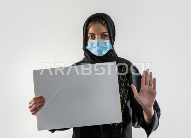 بورتريه لشابة سعودية تضع الكمامة ،  تحمل بيدها لوح ابيض فارغ ، اتباع اجراءات السلامة بوضع الكمامة بشكل صحيح ، تجنب انتشار العدوى ، خلفية بيضاء