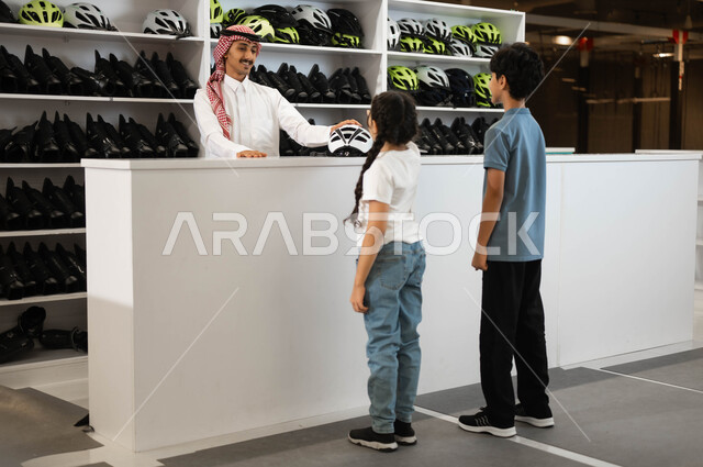 ممارسة الهوايات المفضلة في ساحات التزلج، القيام بطلب استعارة الزلاجات وخوذة الحماية من الاستقبال عند مضمار التزلج ،الاستعداد لبدء التحديات والمغامرات، صورة من الخلف لولد وفتاة عربيان خليجيان سعوديان في احد المراكز الترفيهية في السعودية