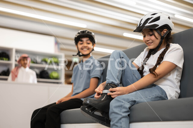 The concept of challenge and competition, developing sports skills in skating rinks, a close-up photo of a Saudi Gulf Arab boy and girl wearing a protective helmet and preparing to conduct exciting experiments in one of the entertainment places in Saudi Arabia, borrowing skates from the reception at the skating track.