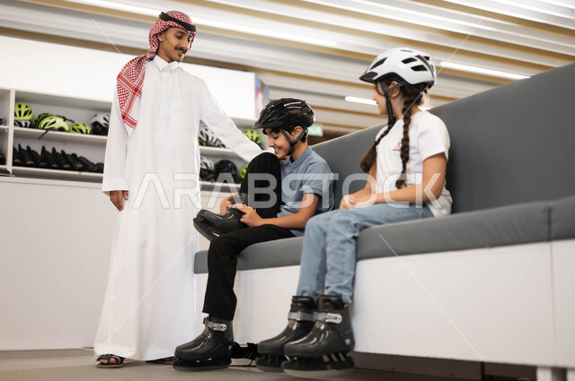 اللعب في ساحات التزلج، قضاء وقت ممتع في تطوير المهارات الرياضية، ايماءات الحماس لبدء السباقات، فتاة و ولد عربي خليجي سعودي يقوم بارتداء الزلاجات و خوذة الحماية، موظف سعودي يقوم بتبادل الأحاديث مع الأطفال بتعابير البشاشة في أحد الأماكن الترفيهيه في السعودية