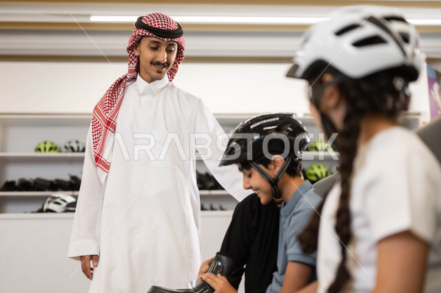ايماءات الحماس لبدء السباقات، صورة مقربة لفتاة و ولد عربي خليجي سعودي يقوم بارتداء الزلاجات و خوذة الحماية، موظف سعودي يقوم بتبادل الأحاديث مع الأطفال بتعابير البشاشة في أحد الأماكن الترفيهيه في السعودية، تطوير المهارات الرياضية في ساحات التزلج
