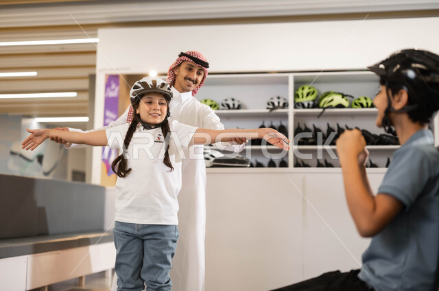 مفهوم الترابط الاسري ،قضاء وقت ممتع مع العائلة في العطلة الصيفيه، رجل عربي خليجي سعودي برفقة أبناءه في أحد الأماكن الترفيهيه في السعودية، ولد وفتاة سعوديان يرتديان خوذة الحماية يستعدان لممارسة هواية التزلج في ساحات الجليد بإيماءات التحدي والمنافسة