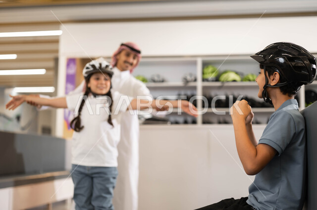 مساعدة الابنة على التوازن ،قضاء وقت ممتع مع العائلة في العطلة الصيفيه، رجل عربي خليجي سعودي برفقة أبناءه في أحد الأماكن الترفيهيه في السعودية، ولد وفتاة سعوديان يرتديان خوذة الحماية يستعدان لممارسة هواية التزلج في ساحات الجليد بإيماءات التحدي والمنافسة