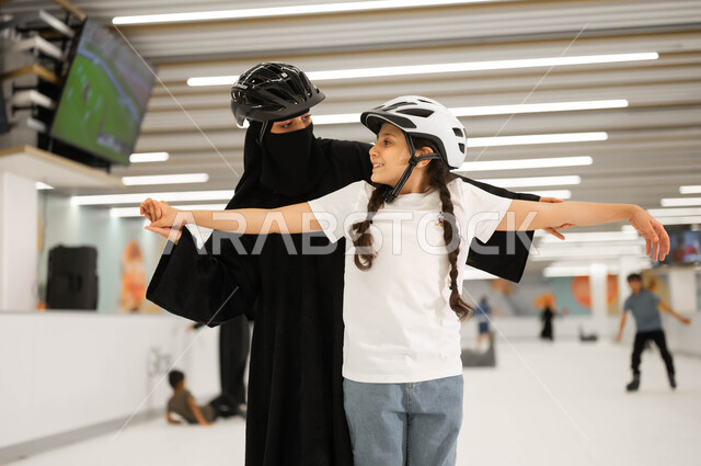المشاركة العائلية في تحقيق النجاح في إحدى الأماكن الترفيهيه، تعليم الابناء على التزلج في ساحات الجليد، مفهوم المحبة و الترابط الأسري، الاهتمام في نفسية الأولاد ومنحهم الطاقة الايجابية، أم عربية خليجية سعودية محجبة تمسك بأيدي ابنتها لتساعدها باللعب بايماءات السرور