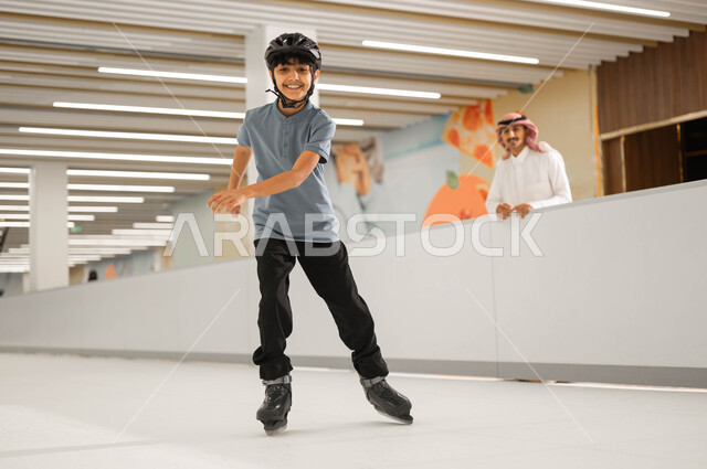 انشطة حركية ترفيهيه للأطفال، الاهتمام بالأبناء ومنحهم الطاقة الايجابية، اللعب في ساحات التزلج على الجليد، ولد عربي خليجي سعودي يرتدي خوذه الحماية ويقوم بممارسة الالعاب المفضلة في إحدى الأماكن المسلية برفقة والده في السعودية، النظر الى الكاميرا بإيماءات الحماس