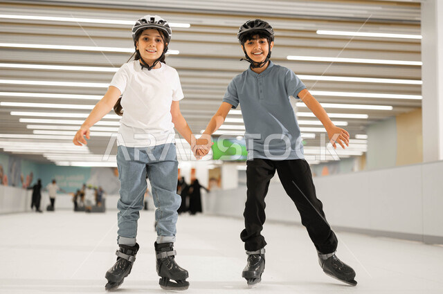 النظر الى الكاميرا بإيماءات السرور ،أجواء عائلية مليئة بالحب، اجراء تجارب مثيرة في مولات السعودية ،ممارسة الألعاب المفضلة في إحدى الأماكن الترفيهيه ،فتاة عربية خليجية سعودية ترتدي خوذة الحماية و تمسك بيد شقيقها وتشاركه في اللعب في ساحات التزلج على الجليد