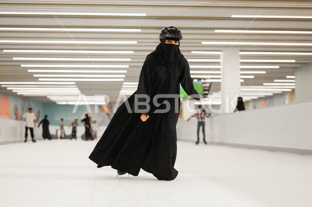 قضاء أوقات الفراغ في اللعب في ساحات التزلج على الجليد في السعودية ،تطوير المهارات الرياضية، امرأة عربية خليجية سعودية محجبة ترتدي العباءة السوداء و خوذة الحماية و تقوم في ممارسة ألعاب التزلج المفضلة في إحدى الأماكن الترفيهيه