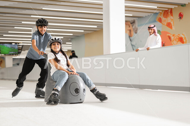 قضاء اجازة ممتعه في العطلة مع العائلة ،اللعب في ساحات التزلج على الجليد، اجراء تجارب مثيرة في مولات السعودية ،ممارسة ألعاب التزلج المفضلة في إحدى الأماكن الترفيهيه ،ولد عربي خليجي سعودي يرتدي خوذة الحماية و يقوم بدفع شقيقته على زلاجة الاطفال