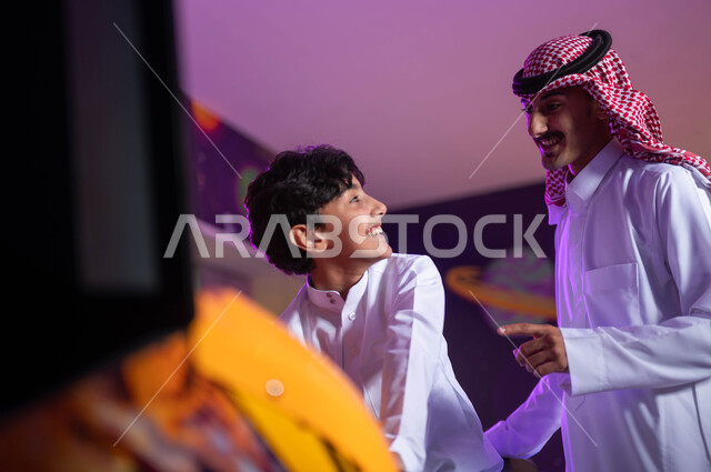 المشاركة في اللعب مع الأبناء، مفهوم الأبوة والبنوة، قضاء وقت ممتع مع العائلة، المراكز الترفيهيه المسلية في السعودية، صورة مقربة لولد عربي خليجي سعودي مع والده يقوم بركوب الدباب الكهربائي المفضل، الاستمتاع بألعاب الاركيد الالكترونية.