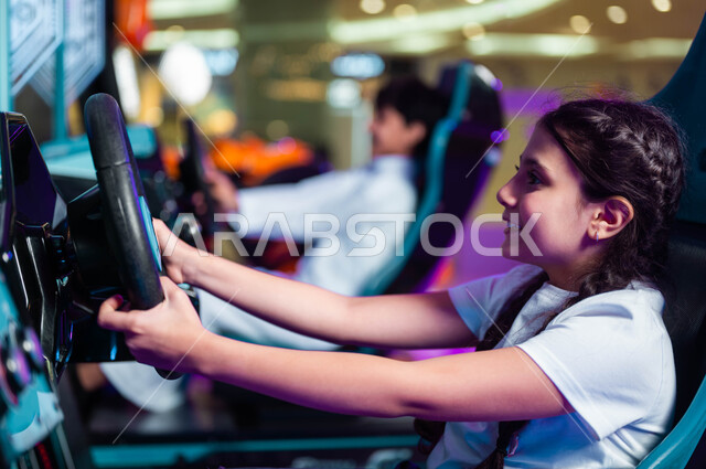Entertainment and pleasure in entertainment centers in Saudi Arabia, a feeling of enthusiasm and joy, a close-up picture from the side of a smiling Saudi Arabian Gulf girl holding the steering wheel playing a car driving simulation game, children’s electric toys, concentration and ability to control