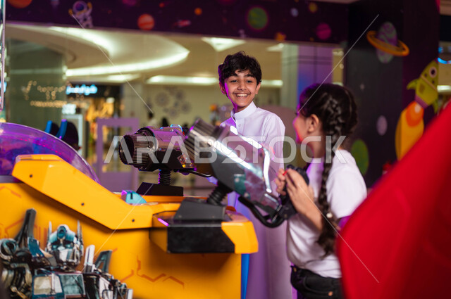 Sharing and playing with brothers, an electronic shooting game, practicing distinct recreational activities, focusing and the ability to control, a Saudi Gulf Arab boy and girl playing advanced arcade games, spending an enjoyable summer vacation.