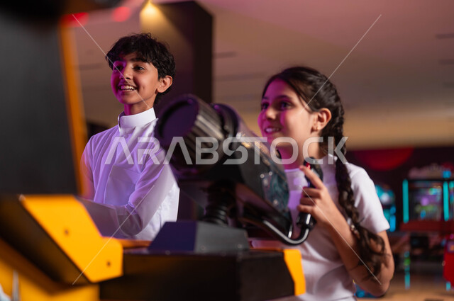 لعبة إطلاق النار الالكترونية، ممارسة الأنشطة الترفيهية المتميزة، التركيز والقدرة على التحكم، ولد وفتاة عربيان سعوديان خليجيان يلعبان ألعاب الأركيد المتطورة، قضاء اجازة صيفيه ممتعة، المنافسات واللعب مع الأخوة.