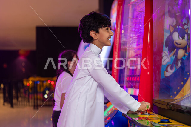 المشاركة والمنافسة في اللعب بين الأخوة، قسم التحديات والمغامرات، الفعاليات الترفيهية في المملكة العربية السعودية، الاستمتاع في قضاء عطلة صيفية ممتعة، ولد عربي سعودي خليجي يلعب مع أخته في ألعاب الأركيد الالكترونية، الشعور بالمتعة والفرح .