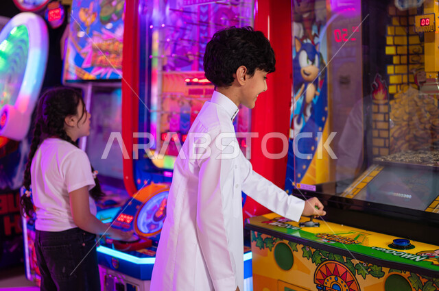 قسم التحديات والمغامرات، المنافسة والمشاركة في اللعب بين الأخوة، الفعاليات الترفيهية في المملكة العربية السعودية، الاستمتاع في قضاء عطلة صيفية ممتعة، ولد عربي سعودي خليجي يلعب مع أخته في ألعاب الأركيد الالكترونية، الشعور بالمتعة والفرح .