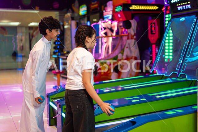 The concept of challenge and competition, the Rolling Sky Ball game, advanced electronic arcade games, amusement and entertainment in Fun Land, a picture from the side of two Saudi Arabian Gulf brothers spending an enjoyable time in the amusement park, the Challenges and Adventures section.