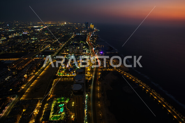 صورة درون جوية لكورنيش مدينة جدة المضاء في الليل، الواجهه البحرية المطلة على ساحل البحر الاحمر، التطور والنمو العمراني للمنشآت وناطحات السحاب, معالم واماكن جذب سياحية في المملكة العربية السعودية، 