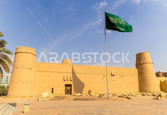 Heritage landmarks of Riyadh, the Saudi flag and the national banner in front of the historic Masmak Castle in the city of Riyadh in broad daylight, the art of architecture and ancient clay buildings, museums and archaeological tourist places in the Kingdom of Saudi Arabia