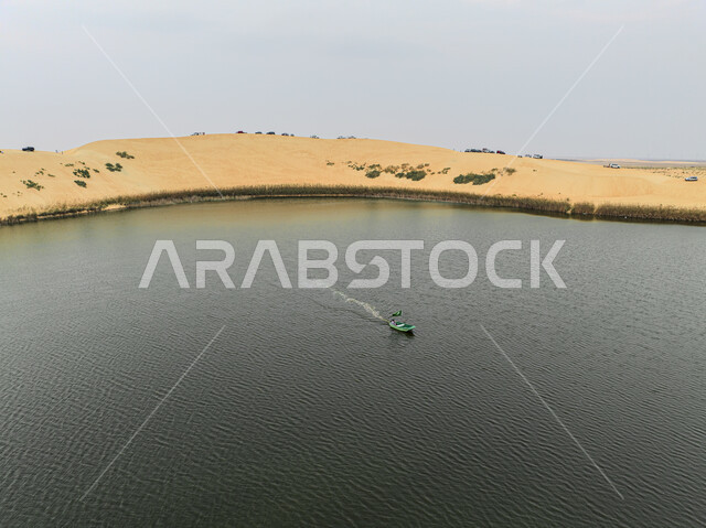 منظر النباتات الخضراء المحيطة بالبحيرات وسط الكثبان الرملية في صحراء المملكة، صورة جوية لقارب صغير وسط بحيرة الأصفر في منطقة الإحساء، مواقع تراثية سعودية عالمية لجذب واستقطاب السائحين من الخارج، أماكن سياحية طبيعية