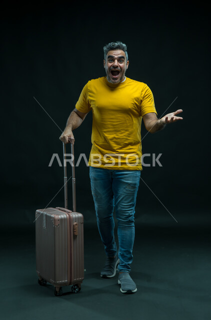 السؤال عن شيء ما بإيماءات الاندهاش، السياحة في إجازة الصيف, الاستعداد لقضاء رحلة صيفية ممتعة, بورتريه لرجل عربي سعودي خليجي يرتدي الزي الكاجوال ينظر إلى الكاميرا يمسك حقيبة السفر, الشعور بالحماس والفرح، صورة الجسم بالطول الكامل, خلفية سوداء.