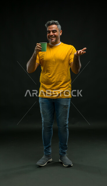 Feeling refreshed and happy, enjoying the good taste of coffee, vitality and activity when drinking caffeine, drinking hot drinks, portrait of a smiling Saudi Arabian Gulf man wearing a casual outfit holding a paper cup in his hand, full-length body portrait, black background