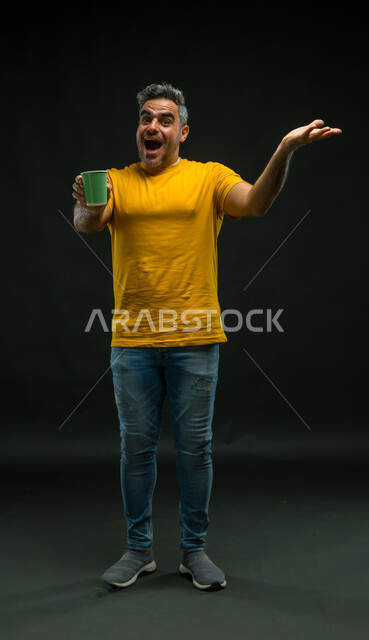 النظر إلى الكاميرا بإيماءات الذهول والتعجب، الاندهاش بالمذاق المتميز للمشروبات الساخنة، تعديل المزاج بتناول الكافيين، بورتريه لرجل عربي خليجي سعودي يرتدي الزي كاجوال يشير بيده إلى كوب من الورق المقوى, صورة لكامل الجسم، خلفية سوداء .