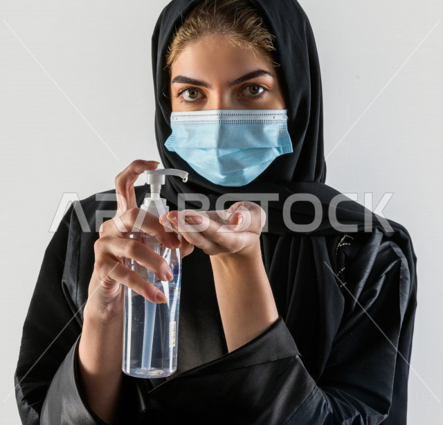 بورتريه لفتاه سعودية تقوم بتعقيم يديها ، ترتدي قناع الوجه ، اتباع اجراءات السلامة باستخدام معقم اليدين ، تجنب انتشار العدوى ، خلفية بيضاء